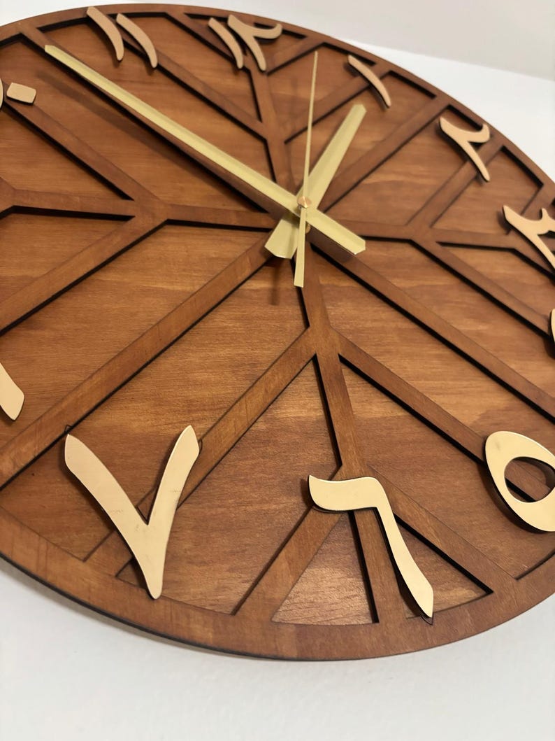 K&ouml;nnte beinhalten: Eine Wanduhr aus Holz mit geometrischem Design. Das Zifferblatt hat eine warme braune Farbe mit goldfarbenen arabischen Ziffern und Zeigern. Das Design weist eine Reihe sich kreuzender Linien auf, die einen einzigartigen und modernen Look erzeugen.