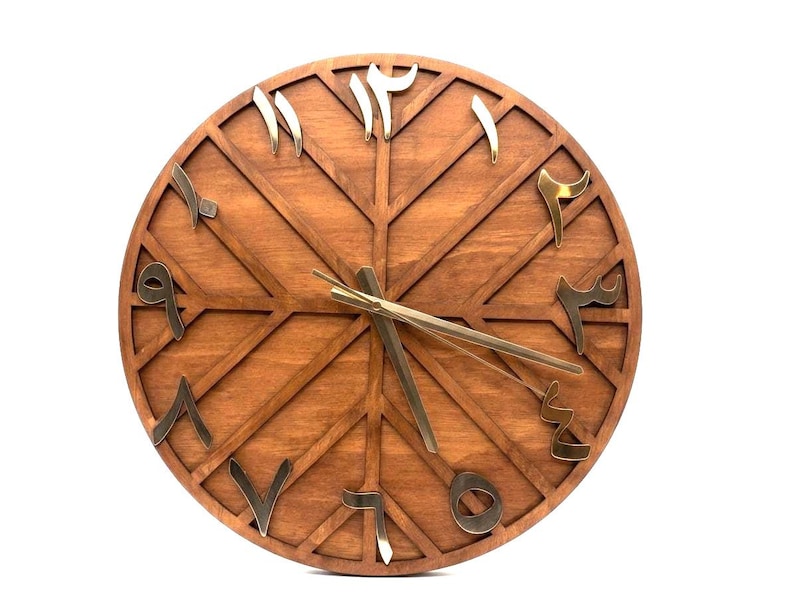 K&ouml;nnte beinhalten: Eine runde Holzuhr mit arabischen Ziffern in Gold. Das Zifferblatt hat eine warme braune Farbe mit einem geometrischen Design. Die Zeiger sind goldfarben und zeigen die Uhrzeit an. Eine dekorative Wanduhr.