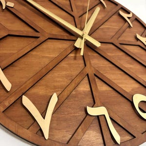 K&ouml;nnte beinhalten: Eine runde Holzuhr mit arabischen Ziffern und goldfarbenen Zeigern. Das Zifferblatt hat ein geometrisches Design mit dunkelbraunem Finish und hellbraunen Akzenten. Die Zeiger zeigen auf 10:08 Uhr.