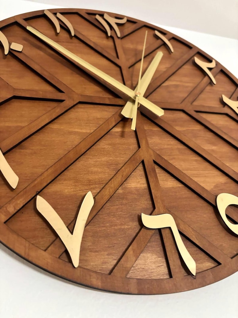 K&ouml;nnte beinhalten: Eine runde Holzuhr mit arabischen Ziffern und goldfarbenen Zeigern. Das Zifferblatt hat ein geometrisches Design mit dunkelbraunem Finish und hellbraunen Akzenten. Die Zeiger zeigen auf 10:08 Uhr.