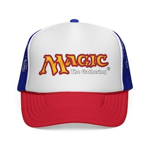 May include: A red, white, and blue trucker hat with the "Magic: The Gathering" logo in yellow and red. The hat has a white front panel with the logo, a red peak, and blue mesh sides and back.
