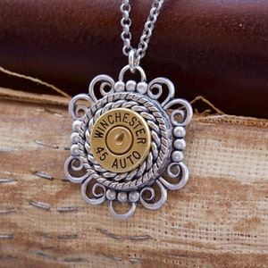 May include: A silver necklace with a gold-toned bullet charm. The bullet is engraved with "Winchester 45 Auto". The charm is surrounded by a silver filigree design.