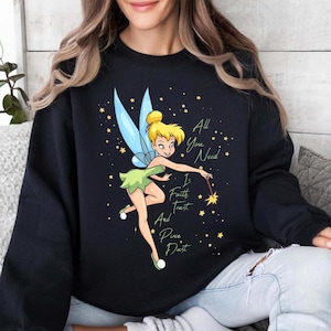May include: Black sweatshirt featuring a cartoon image of Tinkerbell with blue wings and a green dress. The text "All You Need Is Faith Trust And Pixie Dust" is written in white script. Yellow stars are scattered around the fairy.