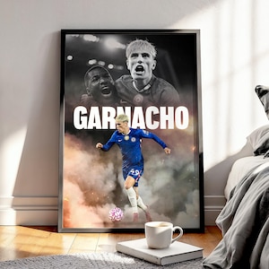 Könnte beinhalten: Gerahmtes Poster mit einem Fußballspieler in blauem Trikot, mit dem Namen "GARNACHO" in Weiß. Das Bild zeigt einen Fußball, eine Tasse Kaffee und ein Buch. Das Poster lehnt an einer Wand.