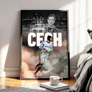 Peut inclure: Affiche encadrée sur le thème du football, représentant un joueur en uniforme bleu et blanc, avec le nom "CECH" en blanc. L'arrière-plan comprend une image en noir et blanc du joueur et un trophée, avec un effet de fumée.