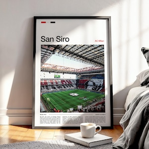May include: Framed poster showing the San Siro stadium, home to AC Milan. The photograph captures the stadium's architecture and the green pitch. The poster includes the text "San Siro" and other text at the bottom. A white coffee cup rests on a book in front of the poster.