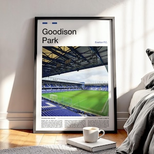 Könnte beinhalten: Gerahmter Druck von Goodison Park, der Heimat von Everton F.C., mit Blick auf das grüne Spielfeld und die blauen Sitzplätze des Stadions. Der Druck enthält den Text "Goodison Park" und "Everton F.C." in minimalistischem Design. Eine weiße Tasse steht auf einem Buch.