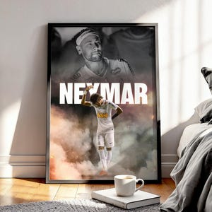 Könnte beinhalten: Ein gerahmtes Poster mit einem Schwarz-Weiß-Bild eines Fußballspielers und dem Namen "NEYMAR" in Weiß. Das Poster hat auch ein Farbbild des Fußballspielers in weißer Uniform. Eine weiße Kaffeetasse steht auf einem Buch.