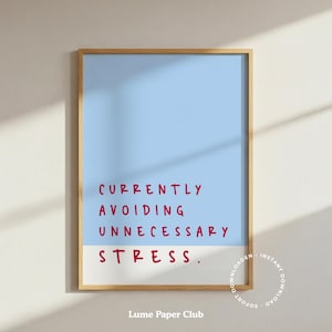 May include: A framed art print with a light blue and white background. The red text reads "CURRENTLY AVOIDING UNNECESSARY STRESS." The print has a wooden frame and is displayed on a white wall.