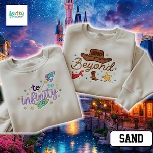 two white sweatshirts with various embroidered designs, including a rocket ship, a castle, and the words "to infinity and beyond" and "sand". The sweatshirts are displayed against a backdrop of a castle and a starry night sky.