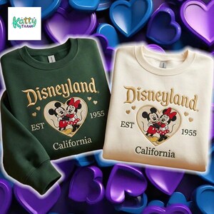 two sweatshirts with the Disney theme park logo and text, set against a background of hearts in various colors.