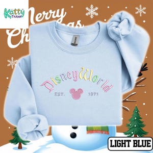 A light blue sweater with the text "Disney World" and "Est. 1971" printed on it, along with a snowman and Christmas trees in the background.