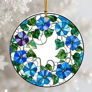 May include: Round ornament featuring a stained-glass design of blue morning glory flowers and green leaves. The flowers are in shades of blue and purple, with a white background. A gold string is attached for hanging.