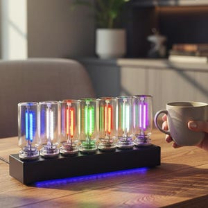 Könnte beinhalten: Eine Digitaluhr mit acht Glasröhren, die farbenfrohe Neonlichter anzeigen. Die Uhr steht auf einem schwarzen Sockel mit blauem Unterlicht, platziert auf einem Holztisch. Der Hintergrund umfasst ein Fenster, einen Stuhl und ein Bücherregal.