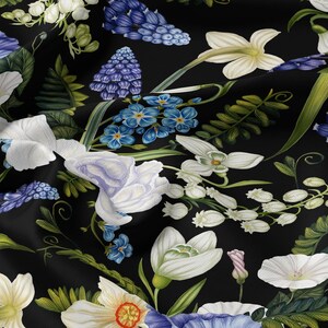 Könnte beinhalten: Ein schwarzer Stoff mit einem dichten, sich wiederholenden botanischen Druck aus weißen Narzissen, blauen Traubenhyazinthen und kleinen hellblauen Vergissmeinnicht mit grünem Blattwerk. Das Material ist drapiert und bildet weiche Falten.