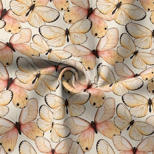 May include: A fabric pattern featuring numerous watercolor butterflies. The butterflies have cream-colored wings with peach and pink accents, and black markings. The background is a light cream color, creating a soft, delicate aesthetic.