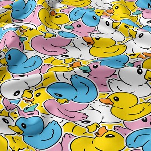 Può includere: Un tessuto con un motivo ripetitivo di paperelle di gomma in stile cartoon nei colori giallo, azzurro, bianco e rosa tenue. Ogni papera è delineata in nero con un becco arancione pieno, disposta in un layout denso e sovrapposto sul tessuto.