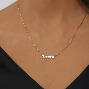 Op de afbeelding: Een goudkleurige ketting met een fijne schakelketting en een centrale naamplaat-hanger met de naam Lauren in een cursief lettertype. Het metaal heeft een gepolijste afwerking die het licht reflecteert voor een heldere, gouden uitstraling.