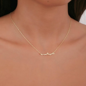 May include: A delicate gold-colored necklace with the name "madison" in cursive script. The necklace is displayed against a neutral background, highlighting the fine details of the jewelry. The chain is thin and elegant, suitable for everyday wear.