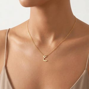 Peut inclure: Un collier doré avec un pendentif en forme de la lettre arabe 'Ain'. Le collier est délicat et suspendu à une fine chaîne. Le pendentif est de conception simple et élégante.