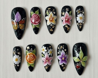 Puede incluir: Un conjunto de diez uñas artificiales negras en forma de almendra. Cada uña presenta un diseño floral o de insectos pintado a mano, incluyendo mariposas, rosas, lirios, margaritas y una mariquita. Los detalles de pan de oro añaden un toque de elegancia al arte de uñas.