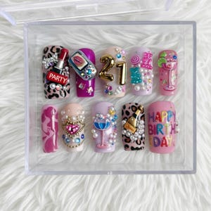 May include: A set of ten artificial nails with various designs, including a lipstick, a phone, the number 21, and the words "PARTY" and "HAPPY BIRTHDAY". The nails feature leopard print, pearls, and cocktail-themed art.