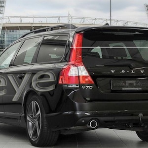 Può includere: Una station wagon Volvo V70 nera con vetri oscurati e cerchi in lega argentati. La parte posteriore dell'auto presenta fanali posteriori rossi e il nome del modello V70. L'auto è parcheggiata di fronte a uno stadio.