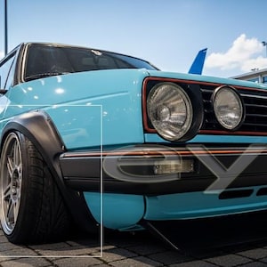 Puede incluir: Un coche clásico azul claro con detalles en negro y una postura baja. El vehículo presenta faros grandes, un alerón delantero negro y llantas de aleación personalizadas. La foto fue tomada al aire libre en un día soleado.
