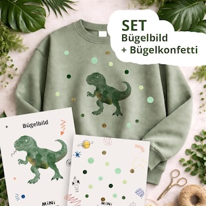 Könnte beinhalten: Ein salbeigrünes Sweatshirt mit einem Aquarell-Dinosaurier-Design und dekorativen Punkten. Das Bild enthält zwei bedruckte Blätter mit Dinosaurier- und Weltraum-Grafiken sowie den Text "SET Bügelbild + Bügelkonfetti".