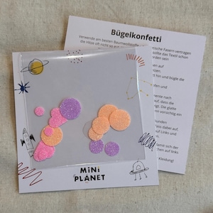 Puede incluir: Un paquete de confeti termoadhesivo en círculos brillantes rosas, naranjas y morados. El paquete tiene un tema espacial con ilustraciones de cohetes y planetas. El texto "Mini Planet" está impreso en el paquete.