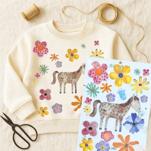 Könnte beinhalten: Cremefarbenes Sweatshirt mit Blumen- und Pferdedesign. Das Sweatshirt zeigt bunte Blumen und eine braune Pferdeillustration. Ein Bogen mit passenden Aufklebern und eine Schere sind ebenfalls vorhanden.