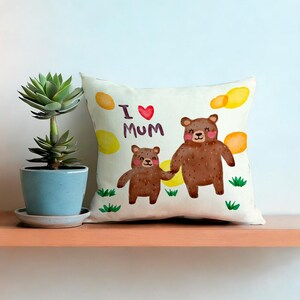 May include: A decorative pillow with a watercolor illustration of two brown bears holding hands. The pillow has the text "I ❤️ Mum" and is decorated with yellow and orange shapes and green grass.