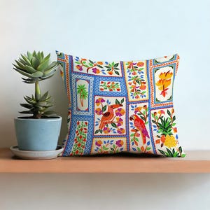 May include: Square decorative pillow with a colorful patchwork design. The pillow features embroidered panels with birds, flowers, and tropical foliage in shades of red, orange, yellow, and blue. The pillow is on a wooden shelf.