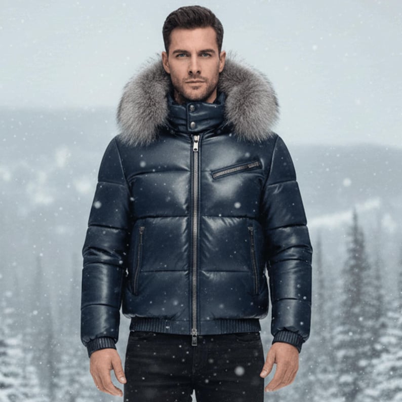 May include: A navy blue puffer jacket with a fur-trimmed hood. The jacket has a zip-up front, multiple pockets, and ribbed cuffs. The model is wearing black jeans. The background shows a snowy winter scene.