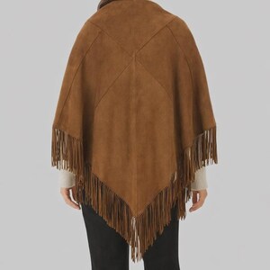 Op de afbeelding: Bruine su&egrave;de poncho met franjes. De poncho heeft een vierkante vorm met een gestikt ontwerp op de rug. De franjes hangen langs de onderkant van de poncho.
