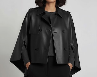 Può includere: Giacca a mantella in pelle nera con doppiopetto, revers a lancia e una silhouette corta e squadrata. La giacca presenta un design a mantella con maniche aperte e dettagli di bottoni. La modella indossa un maglione grigio e pantaloni neri.