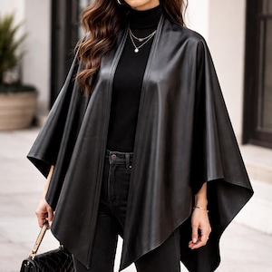 May include: A black faux leather cape with a draped design. The cape is worn over a black turtleneck and black jeans. Accessories include sunglasses, gold hoop earrings, and a small black quilted handbag.