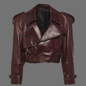 May include: A burgundy leather jacket with a classic trench coat design. The jacket features a notched collar, shoulder epaulets, a belted waist, and adjustable cuffs. The jacket has a single-button closure and a cropped length.