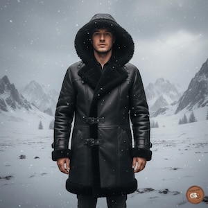 Könnte beinhalten: Ein schwarzer Mantel mit Kapuze, Shearling-Futter und -Besatz. Der Mantel hat einen Schnallenverschluss und wird in einer schneebedeckten Berglandschaft getragen. Der Mantel hat eine lange Länge und ist für kaltes Wetter konzipiert.