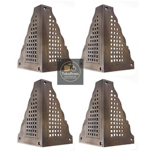 May include: Four bronze-colored, triangular furniture corner brackets. Each bracket features a decorative, openwork design with a series of square cutouts. The brackets are likely made of metal and are designed to reinforce furniture corners.
