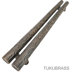 May include: Two bronze-colored, textured door handles with a bark-like appearance. The handles are long and cylindrical, with a slightly curved shape. The handles are made of metal and have a rustic, natural aesthetic.