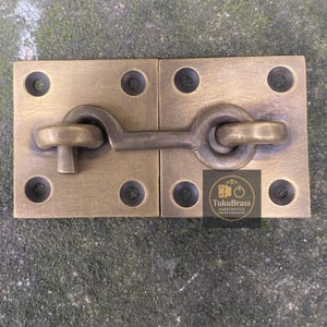 Puede incluir: Un juego de pestillo de gancho y ojo de latón. El juego incluye dos placas cuadradas con esquinas redondeadas y un cierre de gancho y ojo. Cada placa tiene cuatro orificios para tornillos. El pestillo es de color latón cálido.