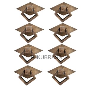 May include: Eight antique brass drawer pulls. Each pull features a diamond-shaped handle within a square frame, mounted on a diamond-shaped backplate. The pulls have a vintage, aged appearance, with a warm, metallic finish.