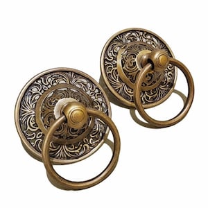 May include: Two antique brass cabinet pulls with a circular design. Each pull features a decorative, engraved face with a ring handle. The pulls have a vintage aesthetic, suitable for furniture restoration or adding a classic touch to cabinetry.