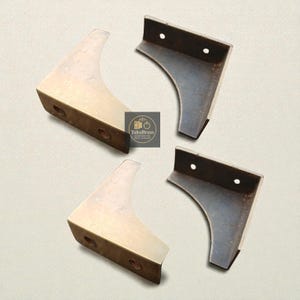 May include: Four brass furniture corner brackets with a curved design. Two brackets are a light gold color, and two are a dark gray color. Each bracket has two pre-drilled holes for mounting. The logo "fukubrass" is in the center.