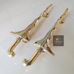 May include: Two brass door handles with an organic, branch-like design. The handles have a curved shape with a textured surface and a polished finish. The handles are mounted on round plates.
