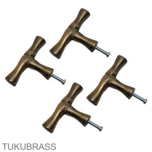 May include: Four brass-coloured cabinet pulls with a T-shaped design. Each pull has a screw for easy installation. The pulls are arranged on a white background. The text "TUKUBRASS" is at the bottom.