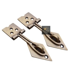 May include: Two antique brass-colored latches. Each latch has a rectangular plate with three holes, connected to a diamond-shaped piece with a rounded roller. The latches are designed for a cabinet or box.
