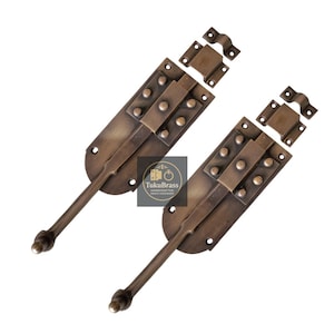 May include: Two antique brass door bolts with matching strike plates. Each bolt features a long handle with a rounded end and is mounted on a rectangular plate with decorative rivets. The bolts are a warm, aged brass color.