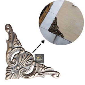 May include: Ornate, antique-style corner bracket in a bronze finish. The bracket features a detailed floral and scroll design, with a small hole for mounting. The image also includes a close-up view of the bracket in a corner setting.